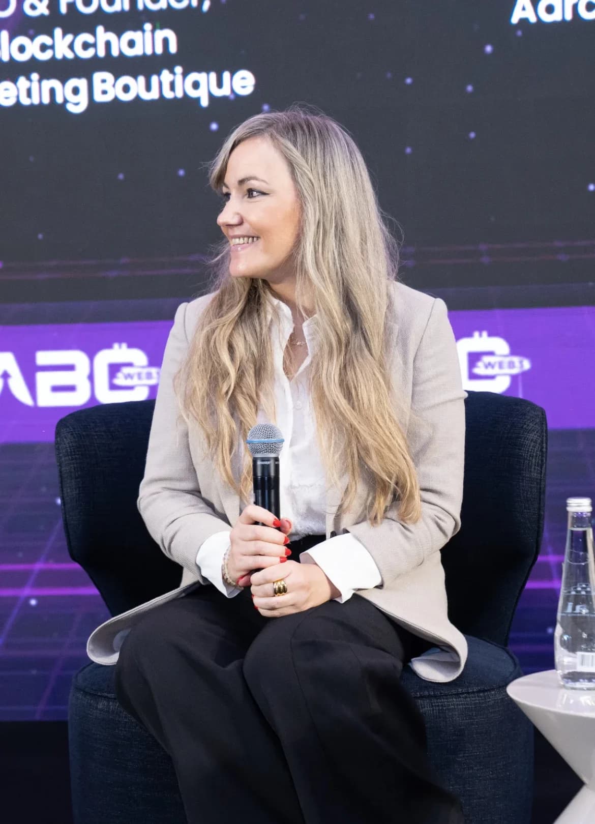 Silvia Mogas seated on stage in Dubai with Blockchain Marketing Boutique on screen