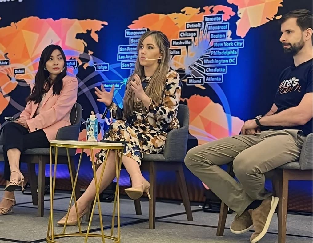 Silvia Mogas speaking on a conference panel in front of a world map of blockchain cities